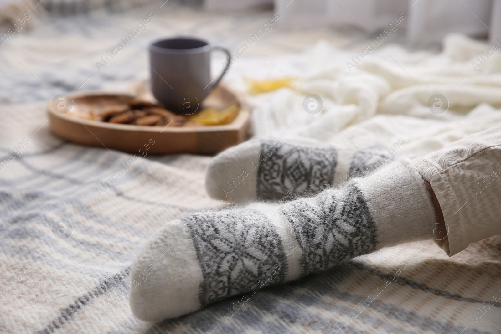 Woman wearing warm socks on knitted plaid, closeup. Cozy season Photo of Woman wearing warm socks on knitted plaid, closeup. Cozy season