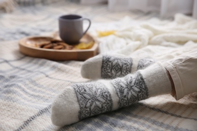 Photo of Woman wearing warm socks on knitted plaid, closeup. Cozy season