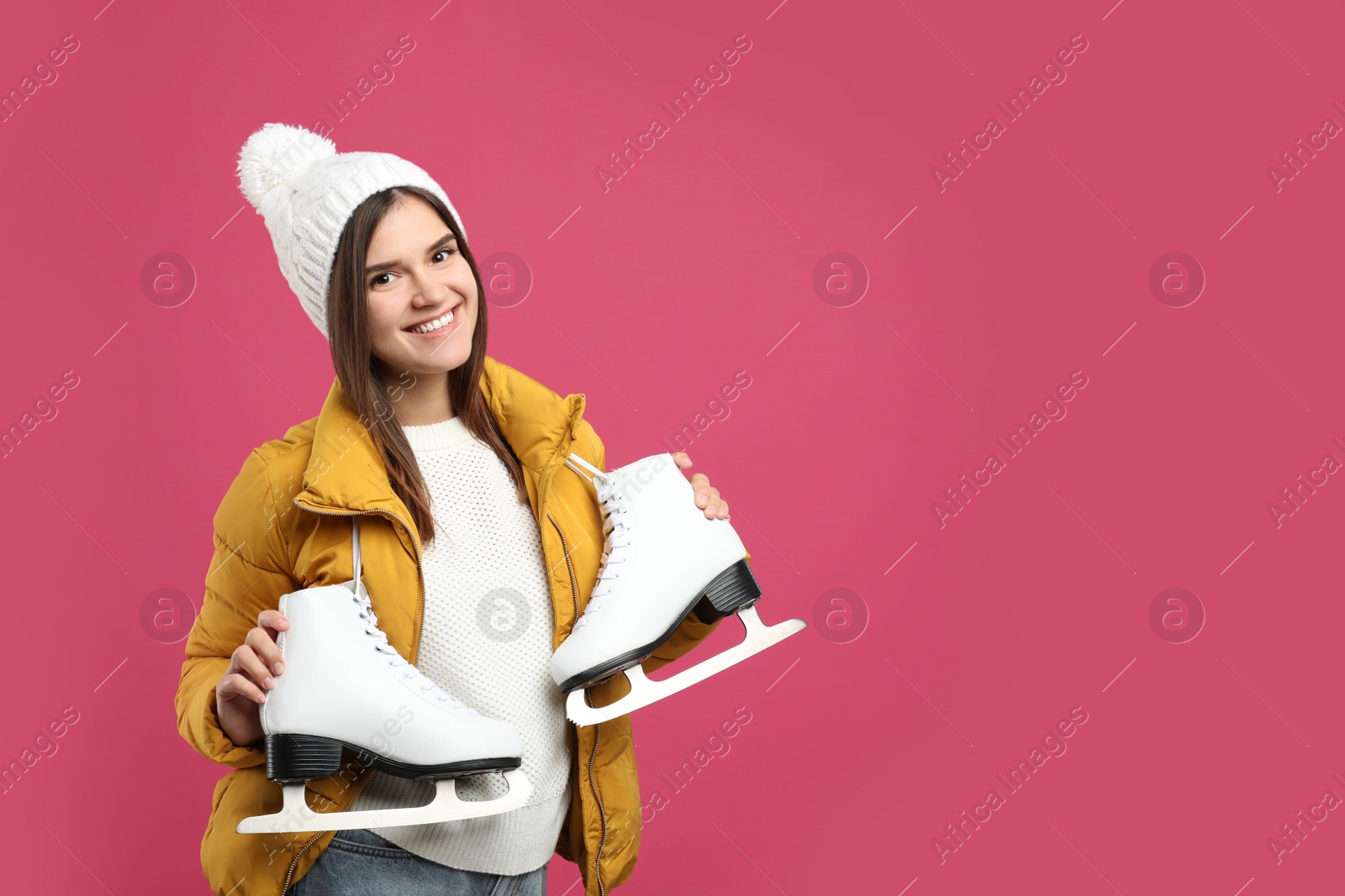 Photo of Happy woman with ice skates on pink background. Space for text