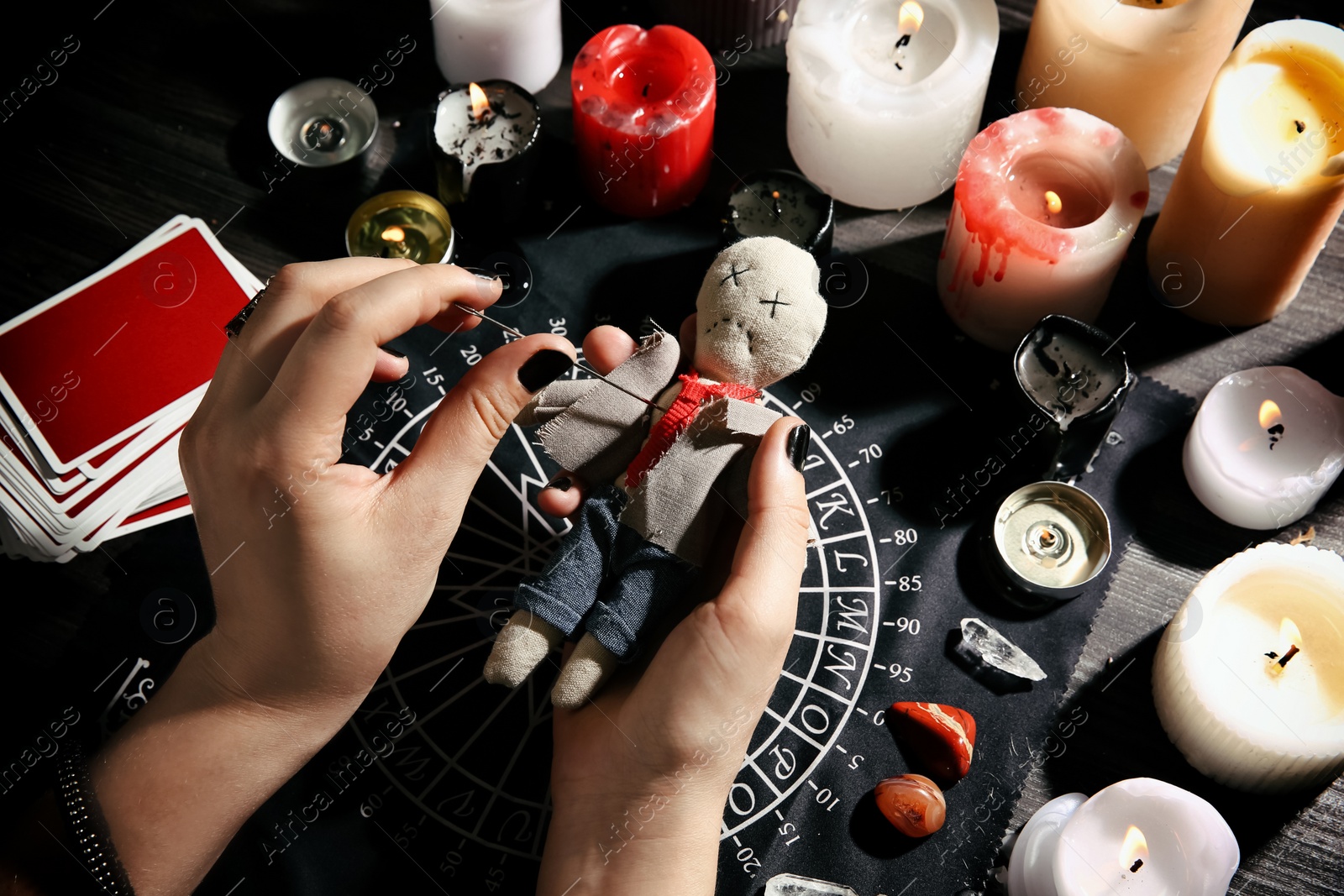 Woman stabbing voodoo doll with needle at table, closeup. Curse ceremony Photo of Woman stabbing voodoo doll with needle at table, closeup. Curse ceremony