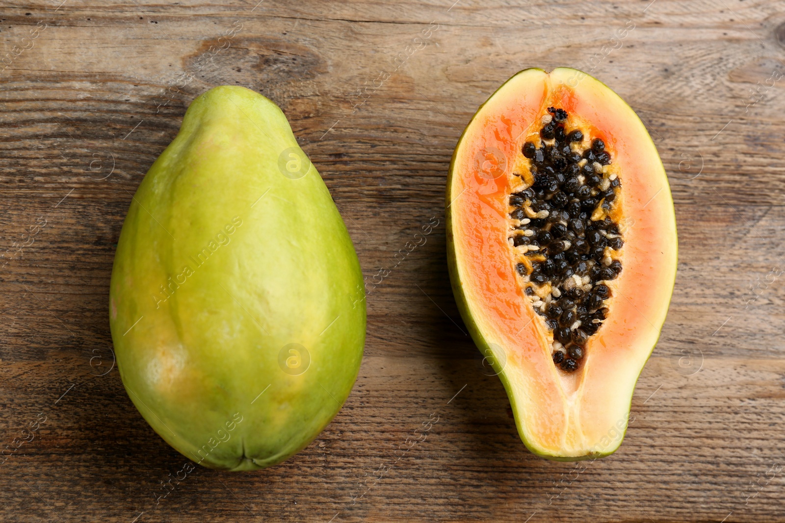 Photo of Cut and whole fresh ripe papaya fruits on wooden table, flat lay