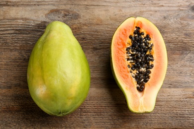 Cut and whole fresh ripe papaya fruits on wooden table, flat lay Photo of Cut and whole fresh ripe papaya fruits on wooden table, flat lay