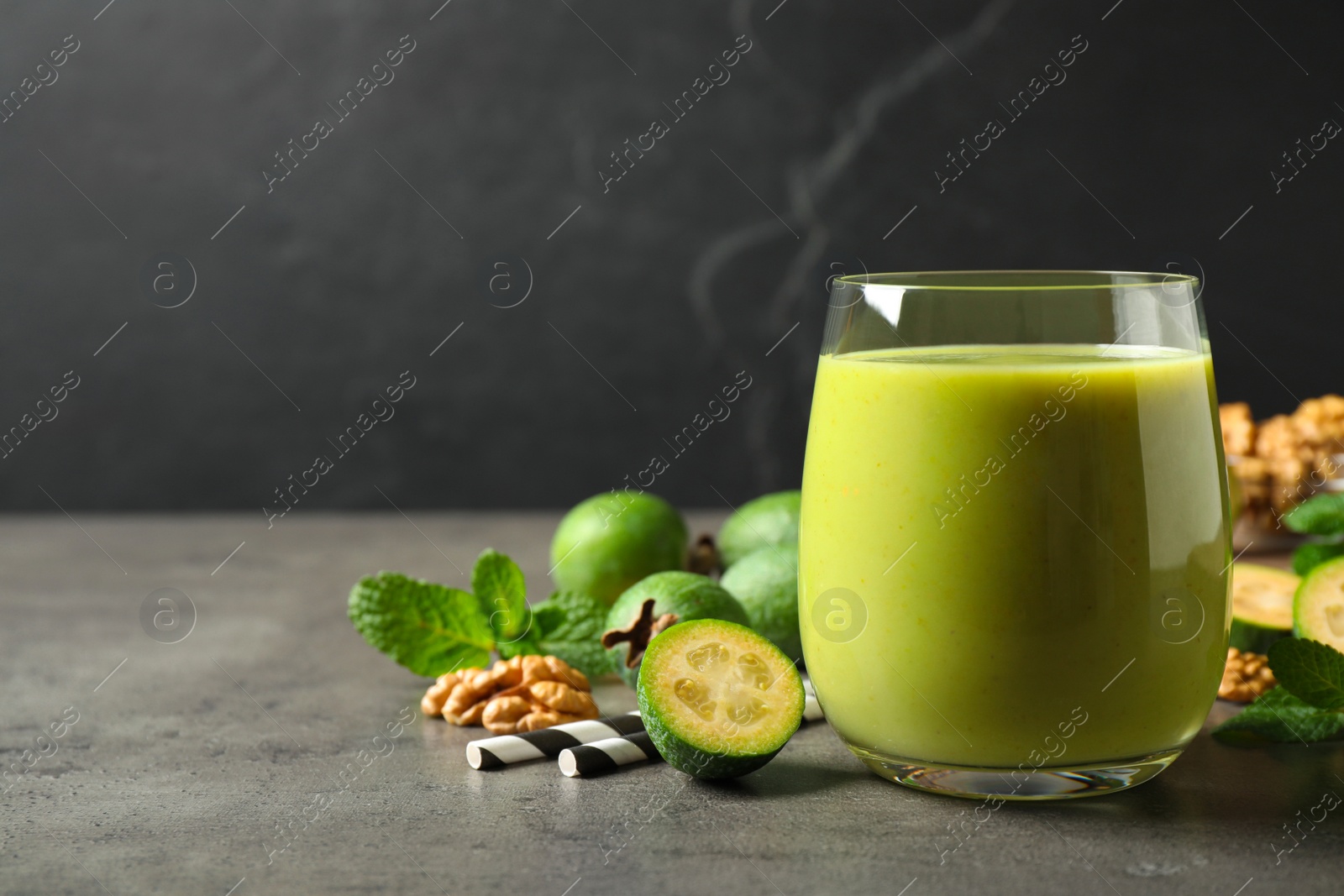 Fresh feijoa smoothie in glass on grey table, space for text Photo of Fresh feijoa smoothie in glass on grey table, space for text