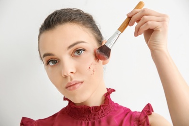 Young woman applying makeup on light background. Professional cosmetic products Photo of Young woman applying makeup on light background. Professional cosmetic products