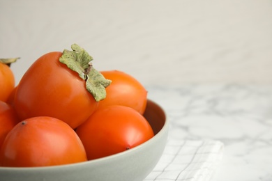 Tasty ripe persimmons in bowl on table, closeup. Space for text Photo of Tasty ripe persimmons in bowl on table, closeup. Space for text