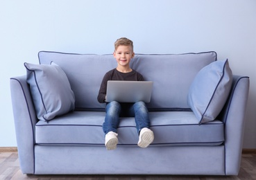 Cute little boy with laptop sitting on sofa, indoors Photo of Cute little boy with laptop sitting on sofa, indoors
