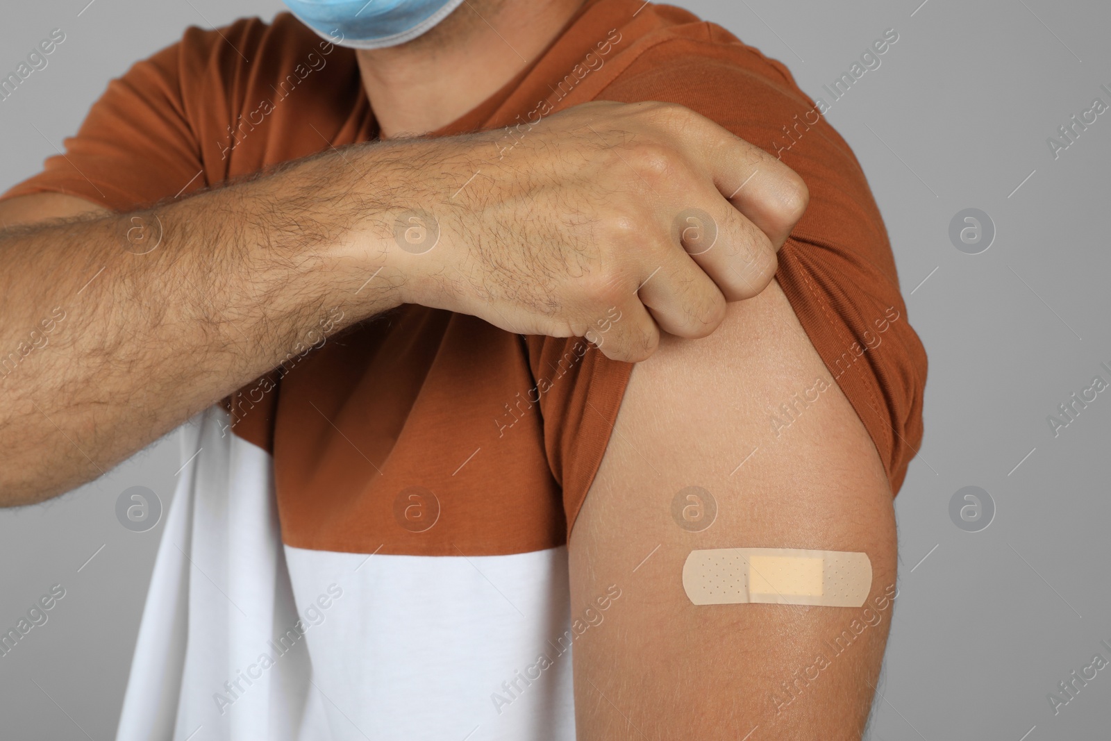 Vaccinated man showing medical plaster on his arm against grey background, closeup Photo of Vaccinated man showing medical plaster on his arm against grey background, closeup