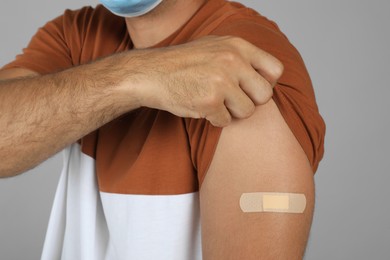 Vaccinated man showing medical plaster on his arm against grey background, closeup Photo of Vaccinated man showing medical plaster on his arm against grey background, closeup