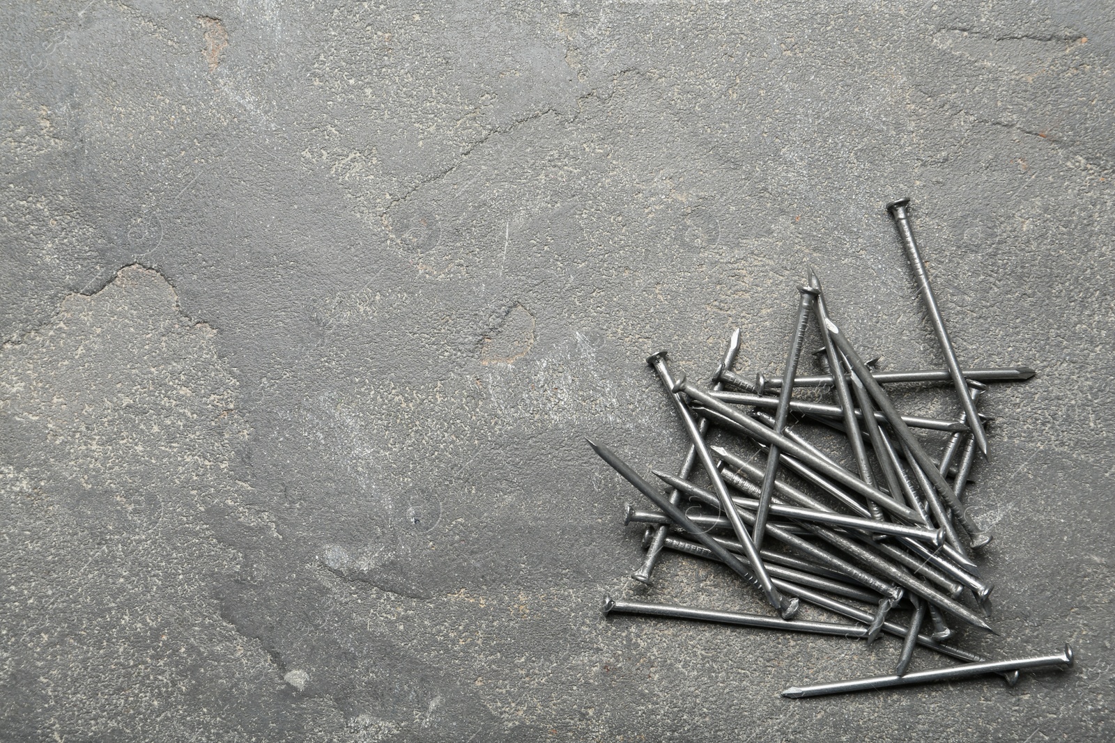 Pile of metal nails on grey stone background, flat lay. Space for text Photo of Pile of metal nails on grey stone background, flat lay. Space for text