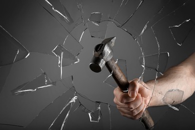 Man breaking window with hammer on dark grey background, closeup Image of Man breaking window with hammer on dark grey background, closeup