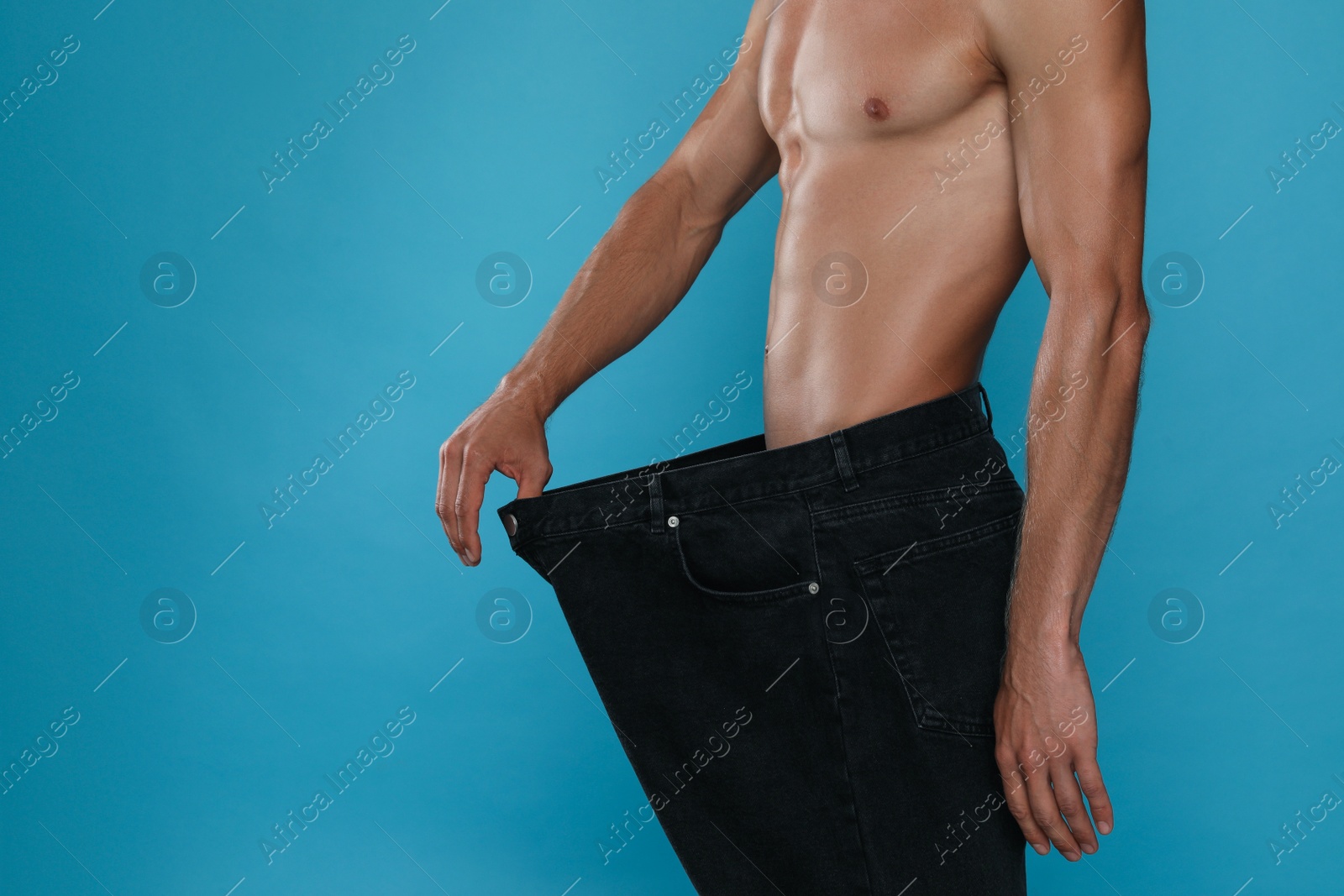 Shirtless man with slim body wearing big jeans on light blue background, closeup Photo of Shirtless man with slim body wearing big jeans on light blue background, closeup