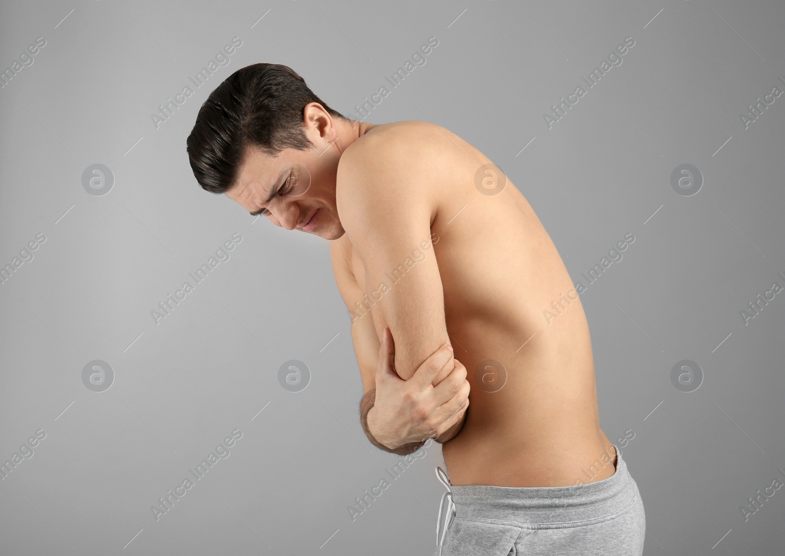 Young man suffering from pain in elbow on grey background Photo of Young man suffering from pain in elbow on grey background