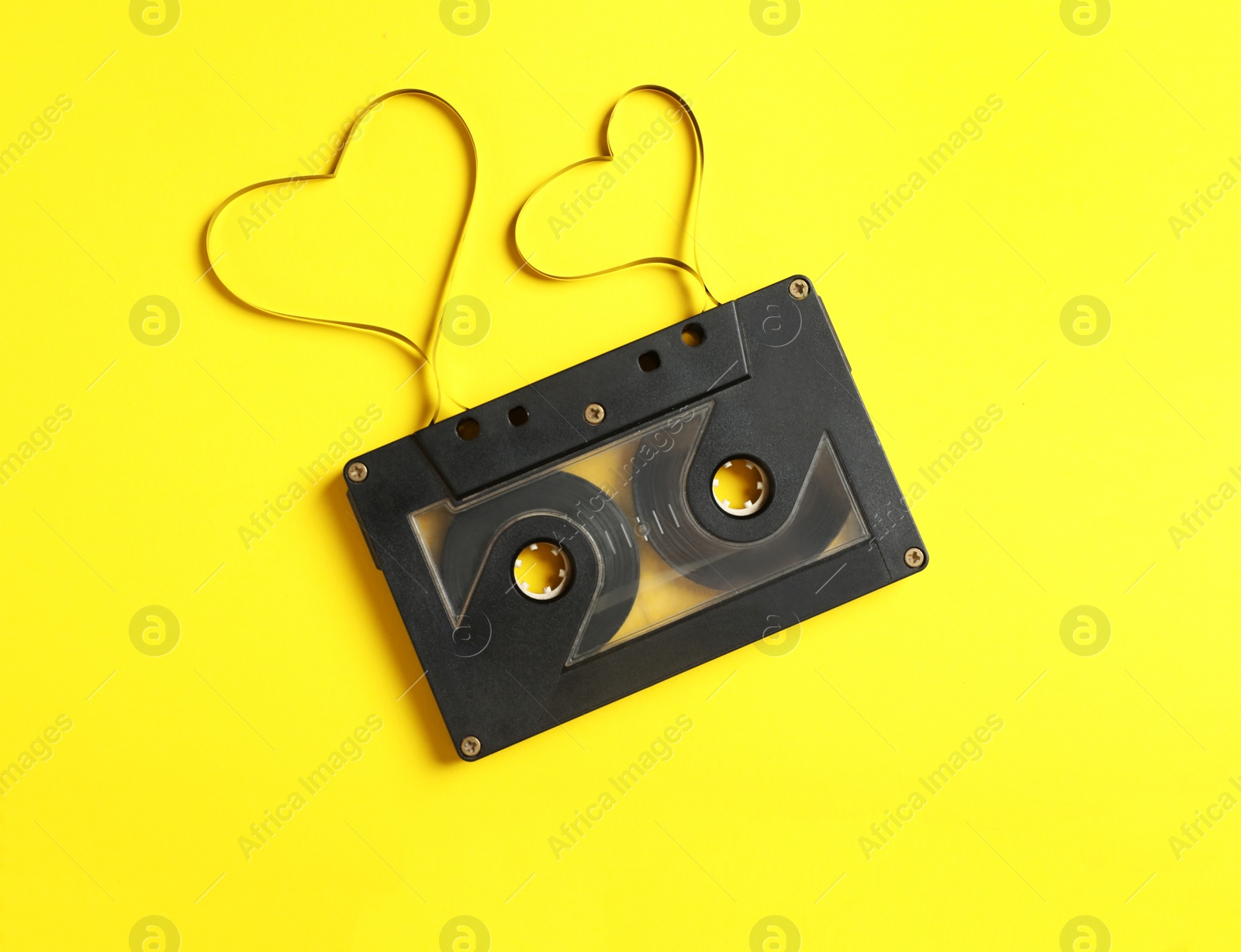 Music cassette and hearts made with tape on yellow background, top view. Listening love song Photo of Music cassette and hearts made with tape on yellow background, top view. Listening love song