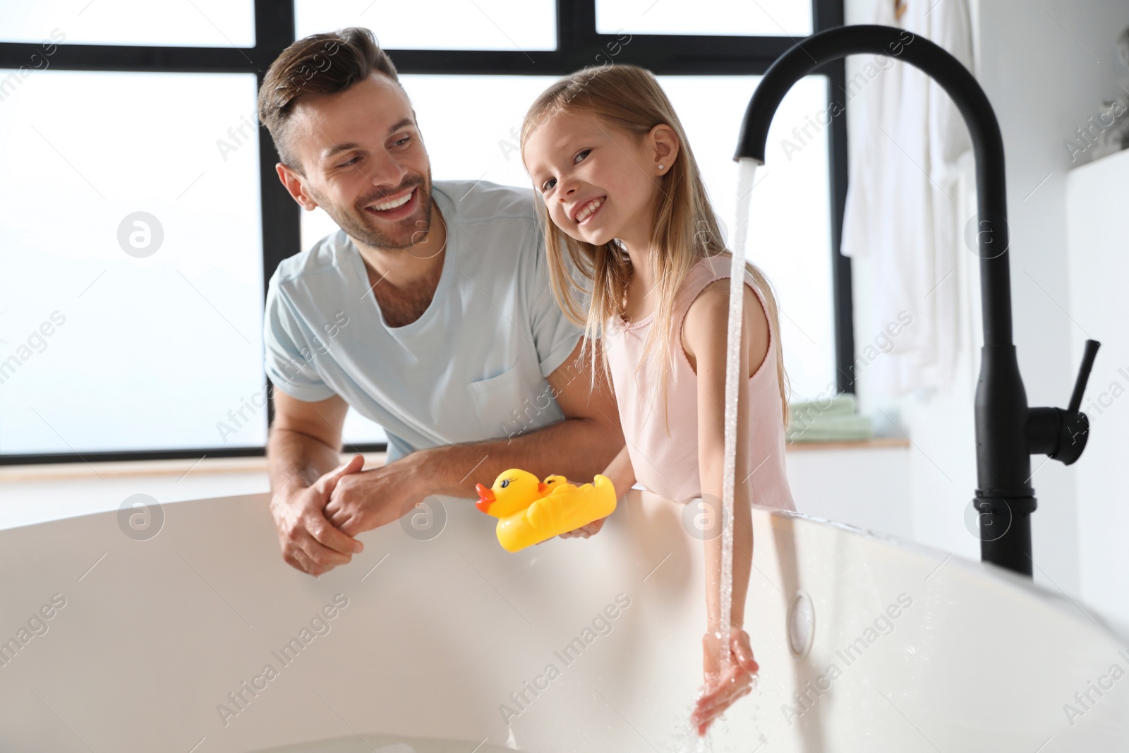 Father with his cute little daughter filling tub in bathroom Photo of Father with his cute little daughter filling tub in bathroom
