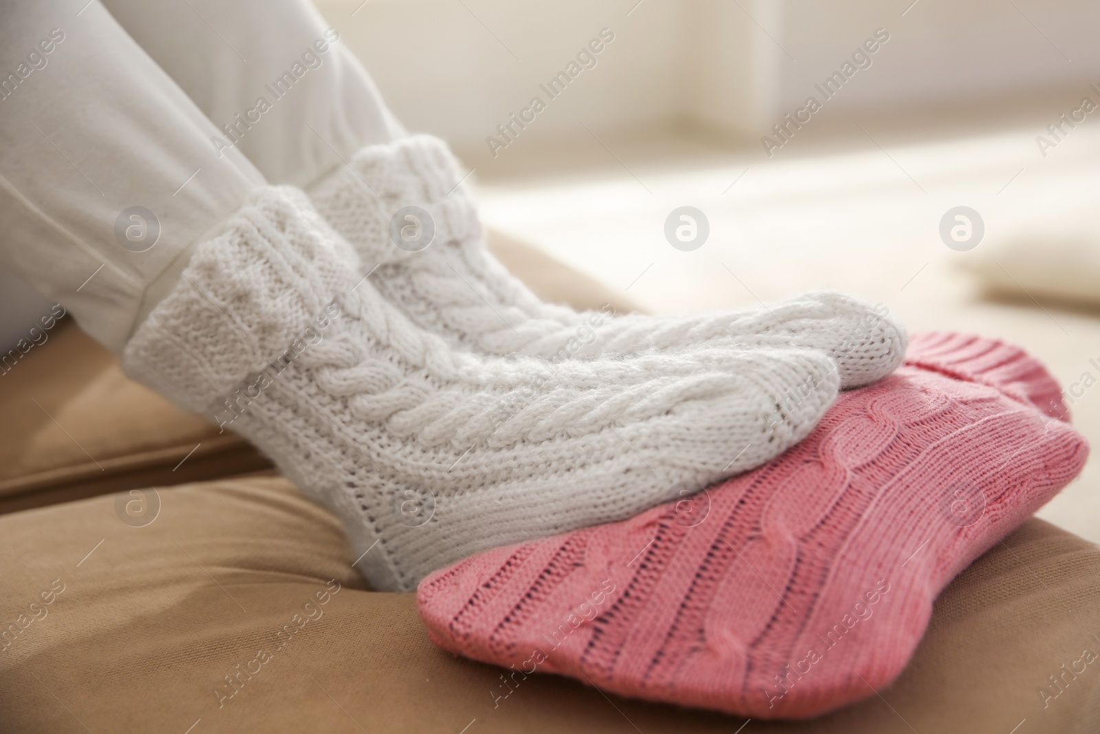 Person warming feet with hot water bottle on sofa, closeup Photo of Person warming feet with hot water bottle on sofa, closeup