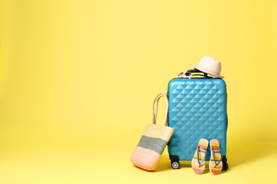 Photo of Blue suitcase with beach accessories on yellow background. Space for text