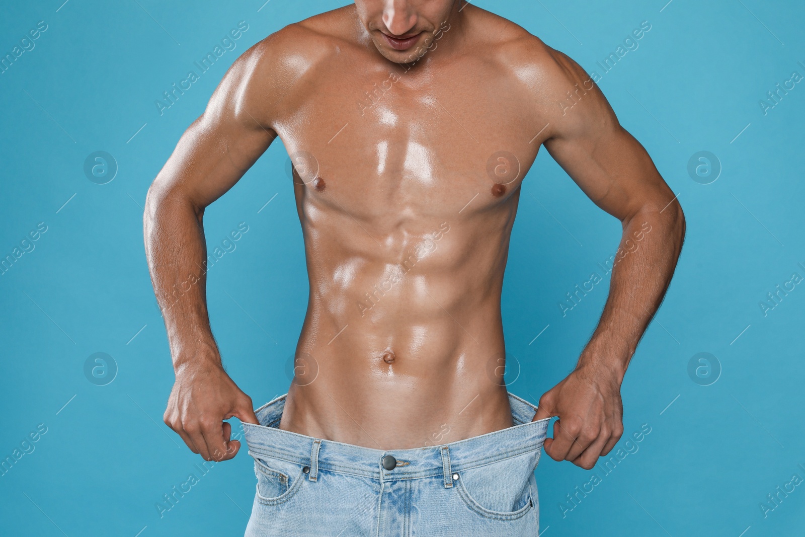 Photo of Shirtless man with slim body wearing big jeans on light blue background, closeup