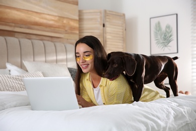 Young woman with eye patches working on laptop near her dog in bedroom. Home office concept Photo of Young woman with eye patches working on laptop near her dog in bedroom. Home office concept