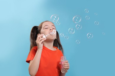 Little girl blowing soap bubbles on light blue background, space for text Photo of Little girl blowing soap bubbles on light blue background, space for text