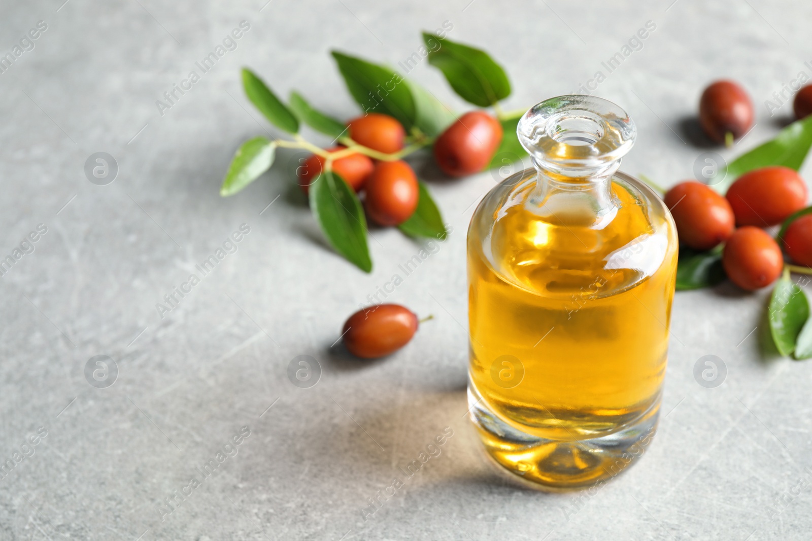 Photo of Jojoba oil in glass bottle and seeds on light grey table
