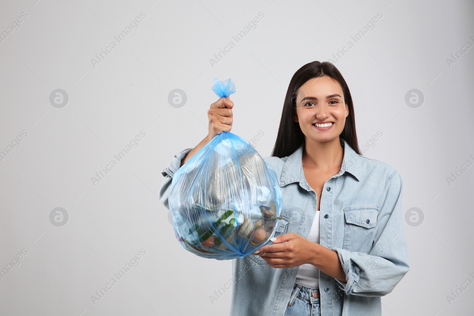 Woman holding full garbage bag on light background Photo of Woman holding full garbage bag on light background