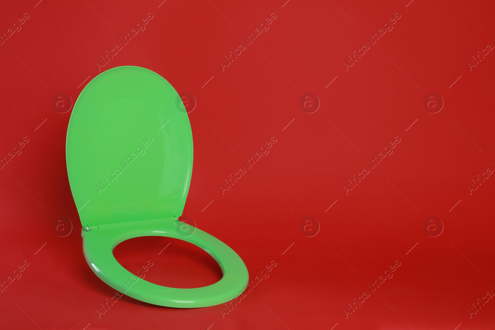 New green plastic toilet seat on red background, space for text Photo of New green plastic toilet seat on red background, space for text