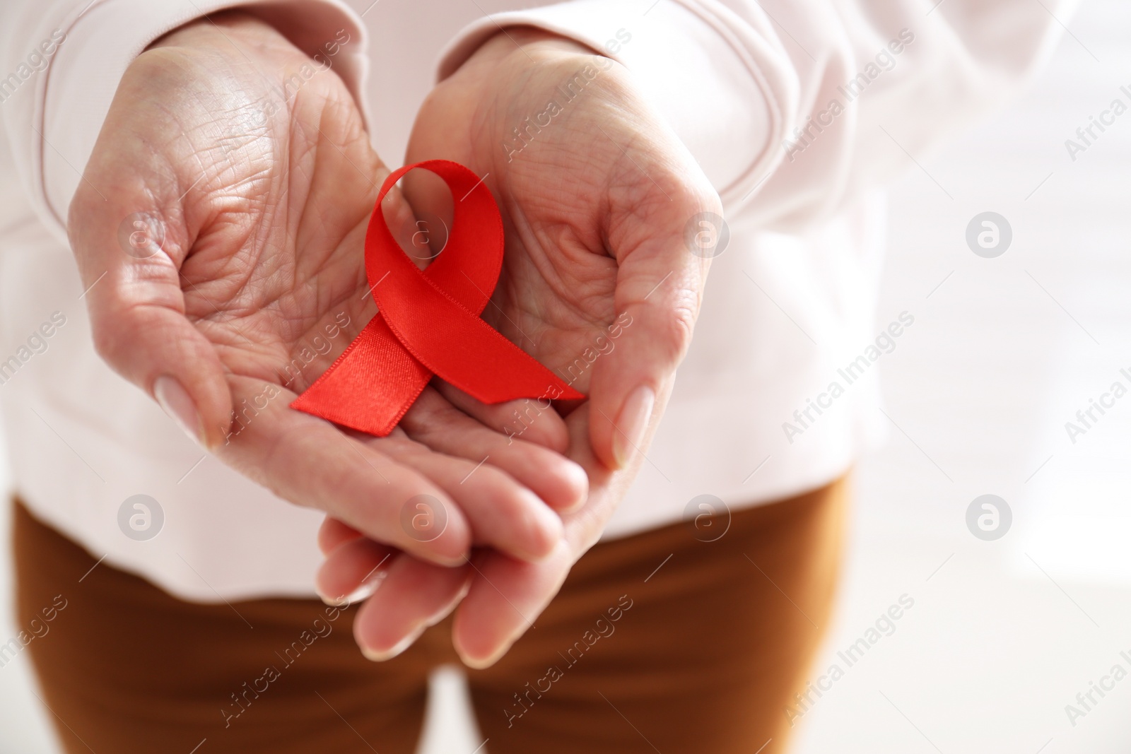 Woman holding red awareness ribbon on light background, closeup. World AIDS disease day Photo of Woman holding red awareness ribbon on light background, closeup. World AIDS disease day