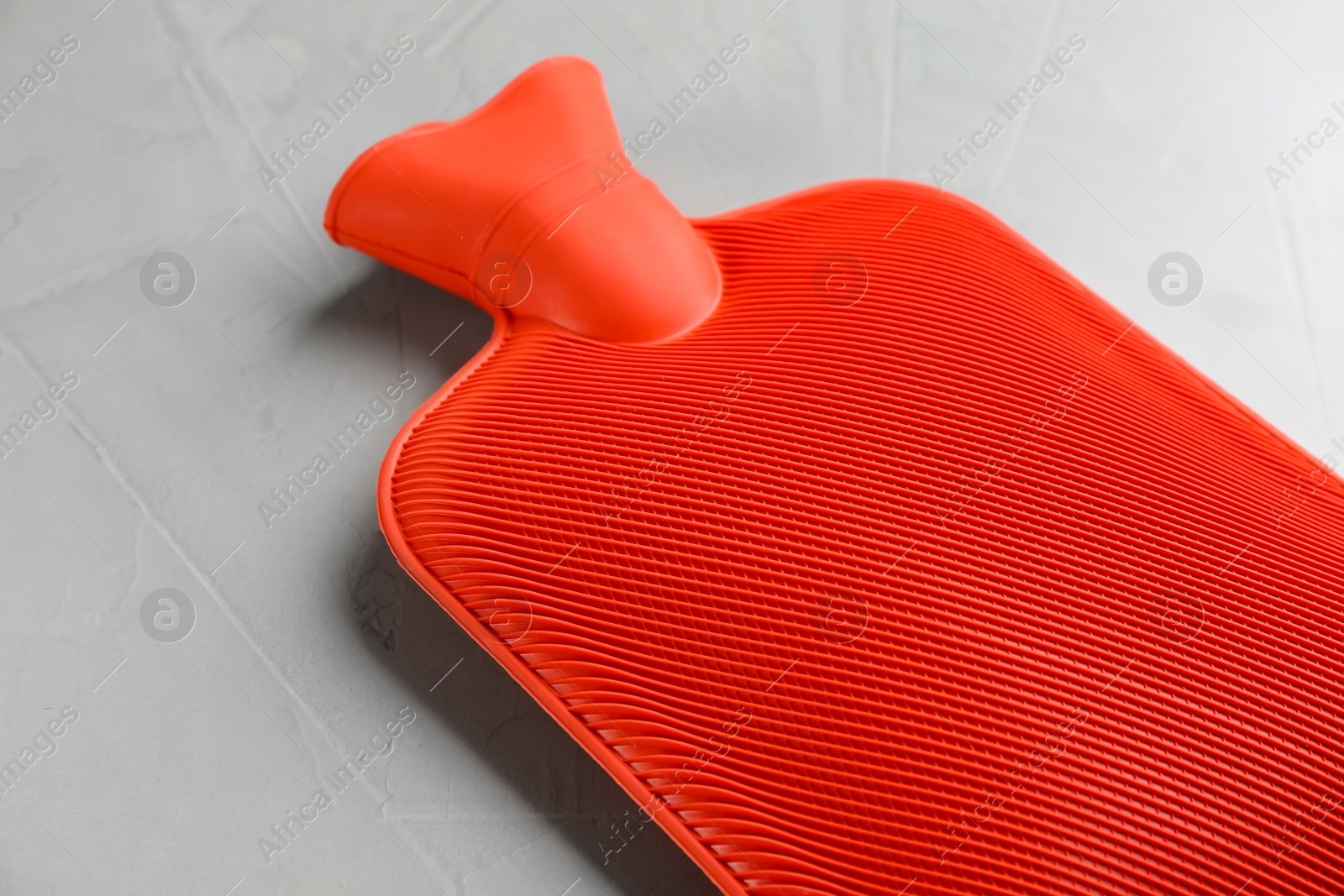 Photo of Red rubber hot water bottle on light grey stone background, closeup