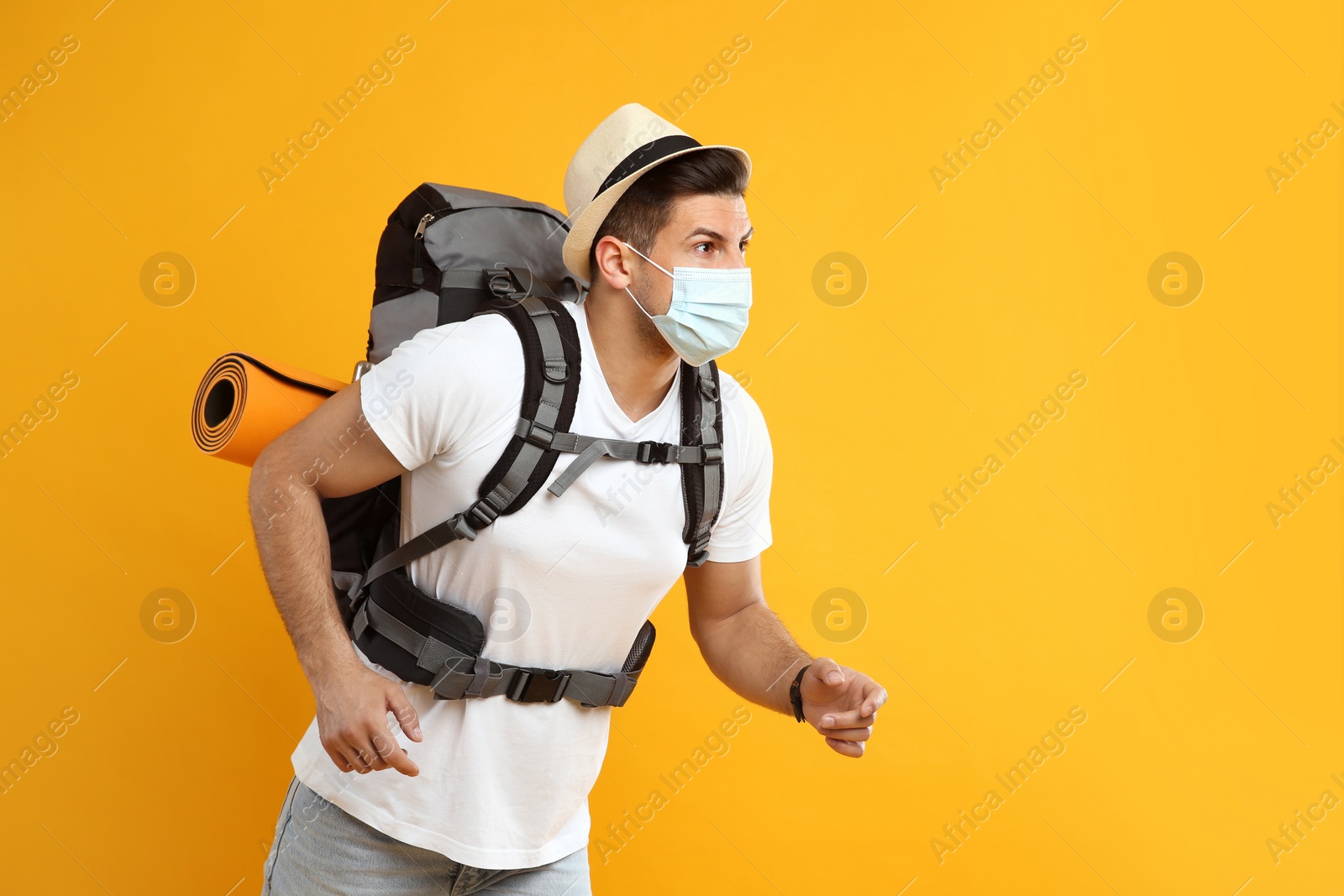 Male tourist in protective mask with travel backpack on yellow background, space for text Photo of Male tourist in protective mask with travel backpack on yellow background, space for text
