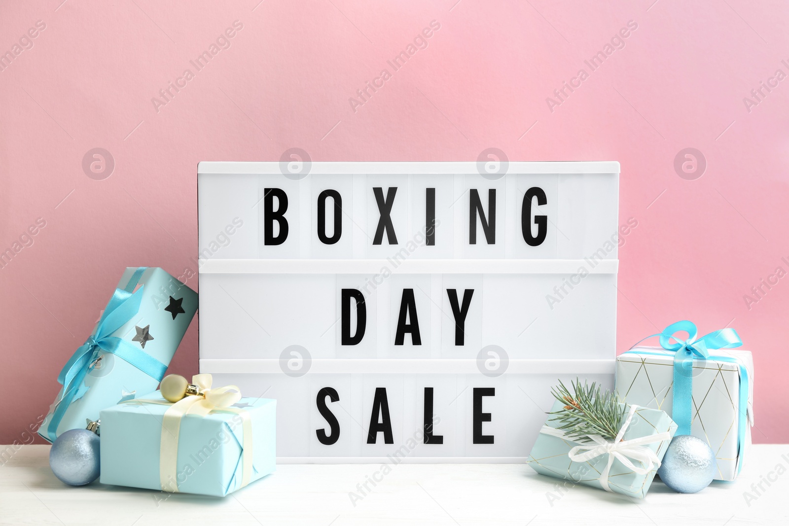 Composition with Boxing Day Sale sign and Christmas gifts on white table against pink background Photo of Composition with Boxing Day Sale sign and Christmas gifts on white table against pink background
