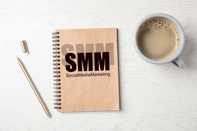 Notebook with text SMM (Social media marketing, cup of coffee and pen on white wooden background, flat lay Image of Notebook with text SMM (Social media marketing, cup of coffee and pen on white wooden background, flat lay