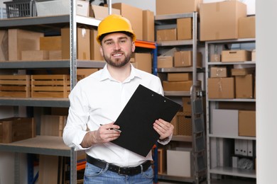 Young man with clipboard near rack of cardboard boxes at warehouse Photo of Young man with clipboard near rack of cardboard boxes at warehouse