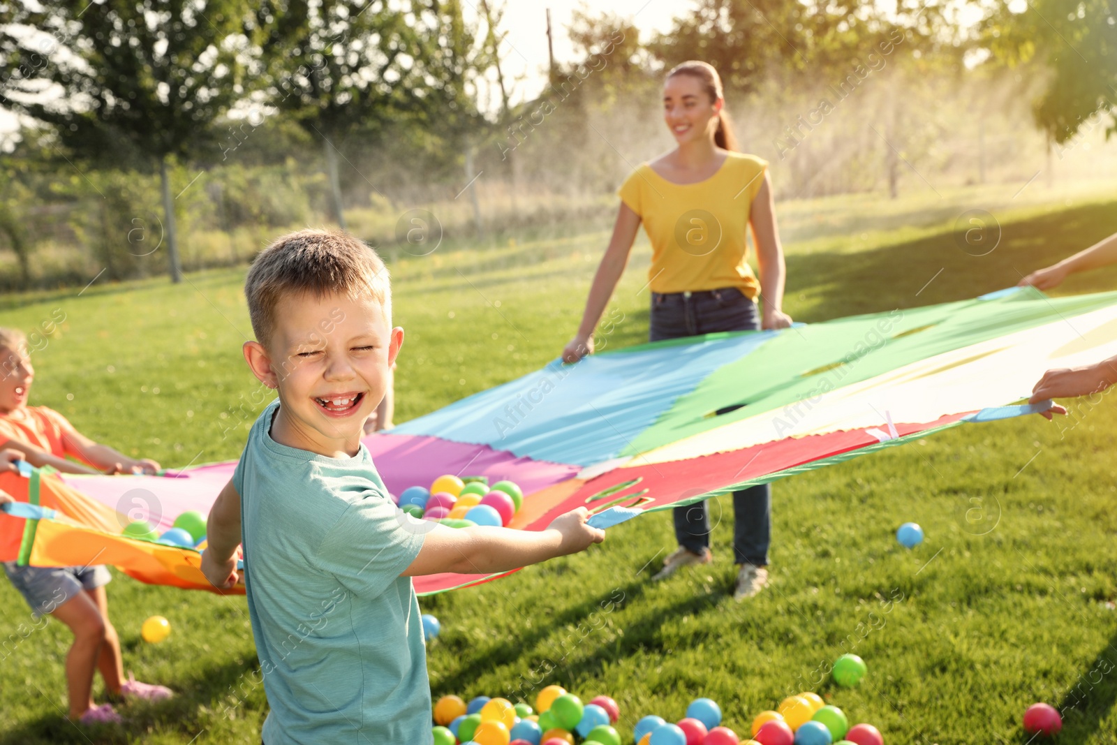 Group of children and teacher playing with rainbow playground parachute on green grass. Summer camp activity Photo of Group of children and teacher playing with rainbow playground parachute on green grass. Summer camp activity