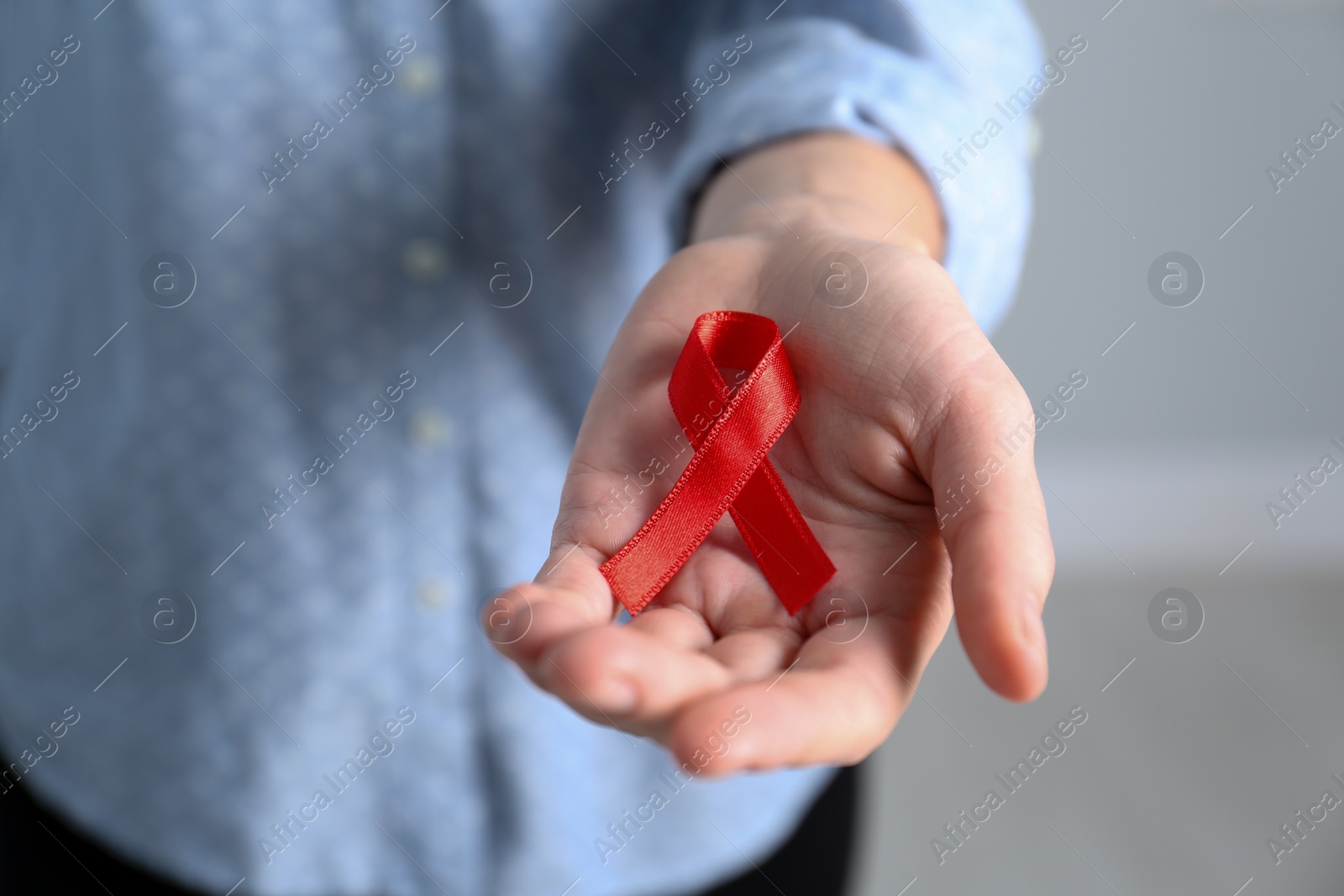 Woman holding red awareness ribbon indoors, closeup. World AIDS disease day Photo of Woman holding red awareness ribbon indoors, closeup. World AIDS disease day