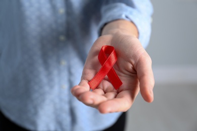 Woman holding red awareness ribbon indoors, closeup. World AIDS disease day Photo of Woman holding red awareness ribbon indoors, closeup. World AIDS disease day