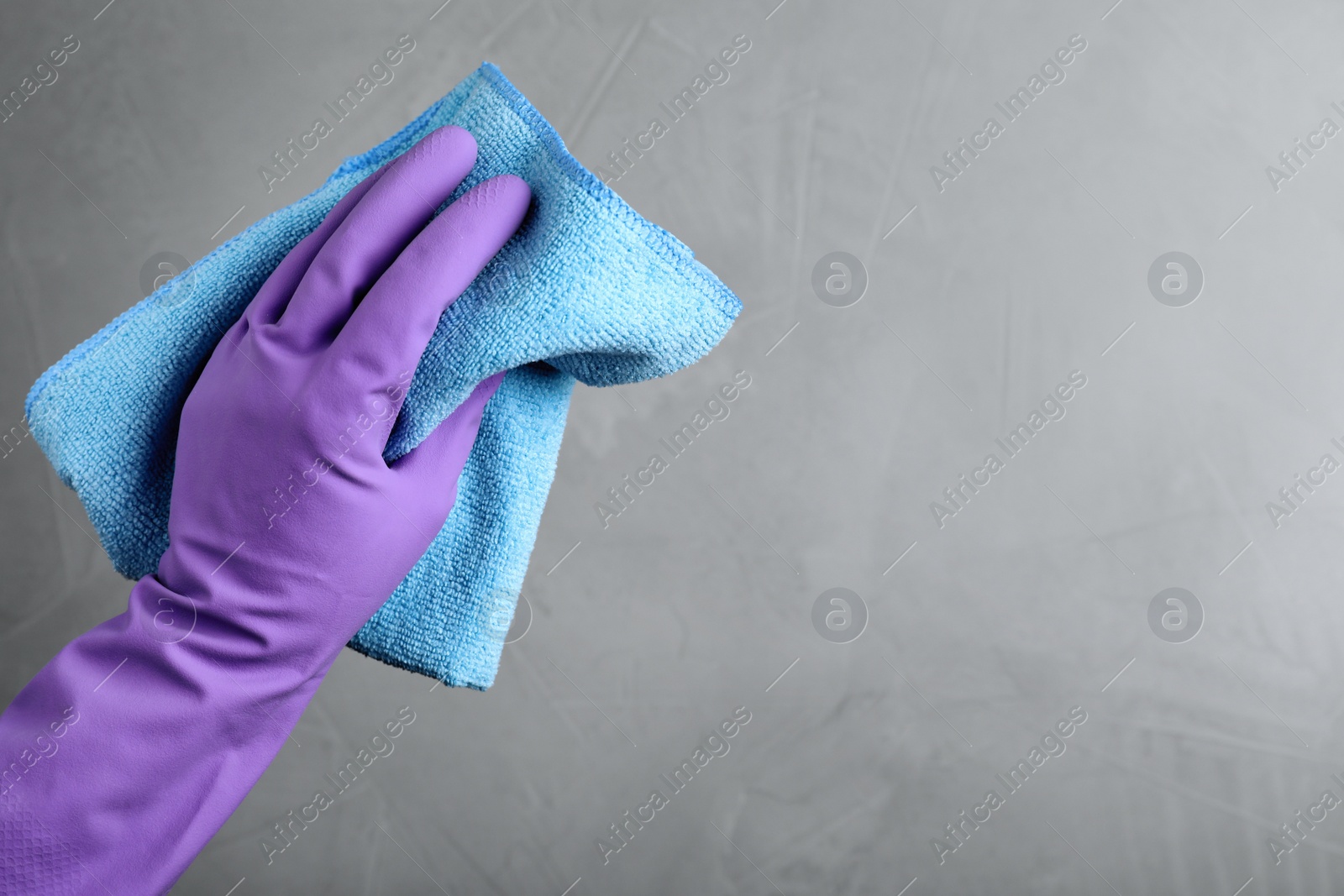 Woman in violet rubber gloves with microfiber cloth on light grey background, closeup. Space for text Photo of Woman in violet rubber gloves with microfiber cloth on light grey background, closeup. Space for text
