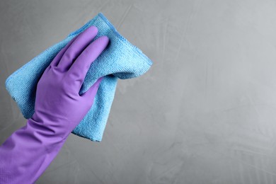 Woman in violet rubber gloves with microfiber cloth on light grey background, closeup. Space for text Photo of Woman in violet rubber gloves with microfiber cloth on light grey background, closeup. Space for text