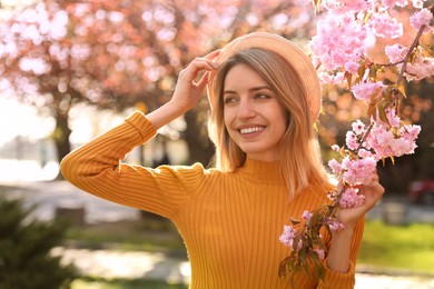 Young woman wearing stylish outfit near blossoming sakura in park. Fashionable spring look Photo of Young woman wearing stylish outfit near blossoming sakura in park. Fashionable spring look