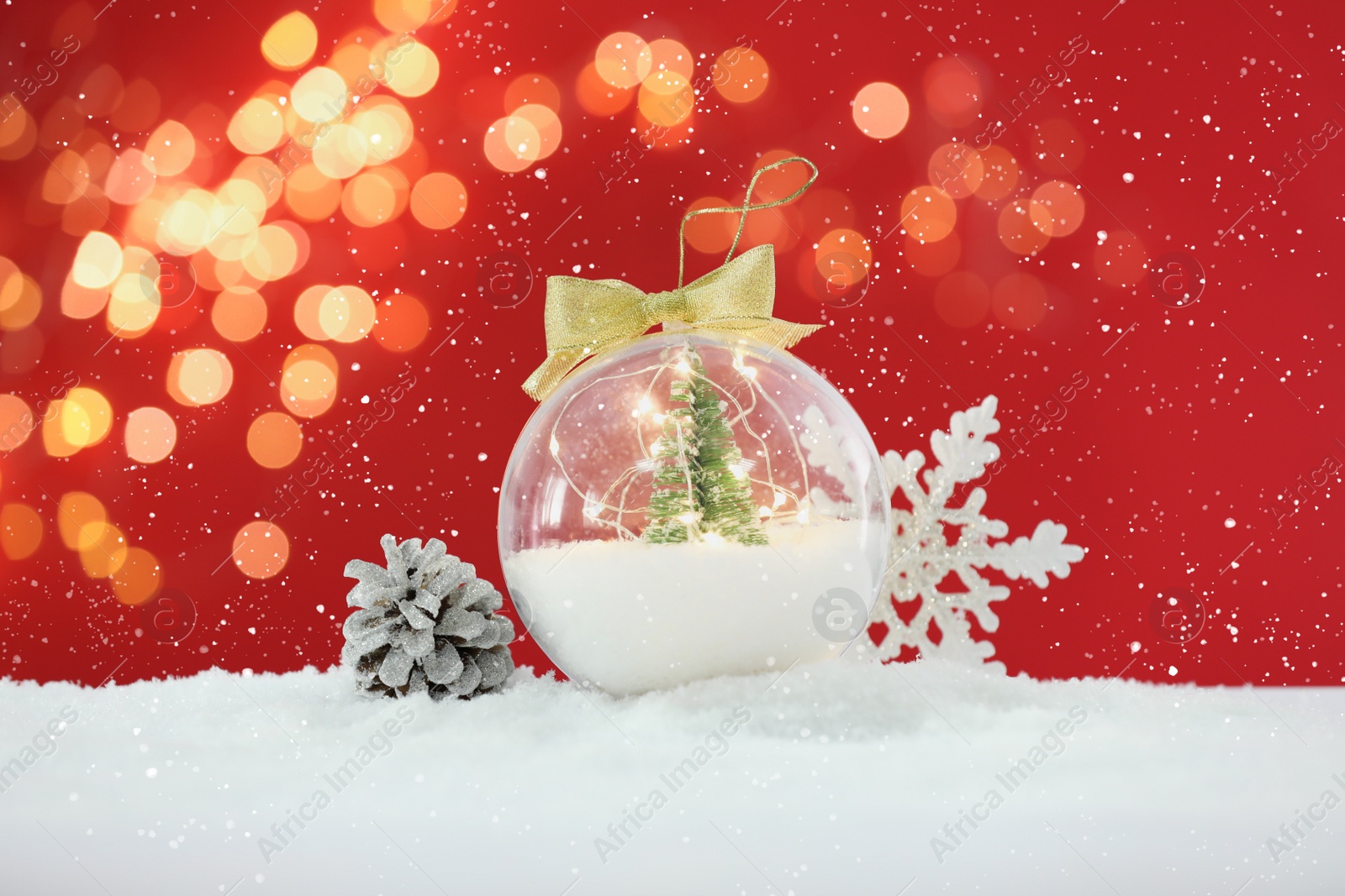 Beautiful transparent Christmas ornament with small fir tree and fairy lights on snow against red background, bokeh effect Image of Beautiful transparent Christmas ornament with small fir tree and fairy lights on snow against red background, bokeh effect
