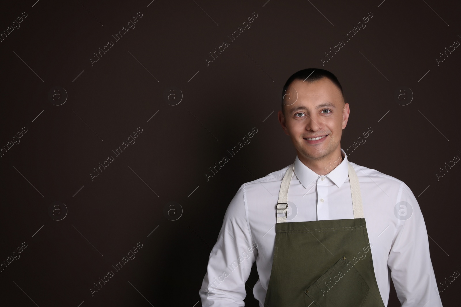 Portrait of happy young waiter in uniform on brown background, space for text Photo of Portrait of happy young waiter in uniform on brown background, space for text