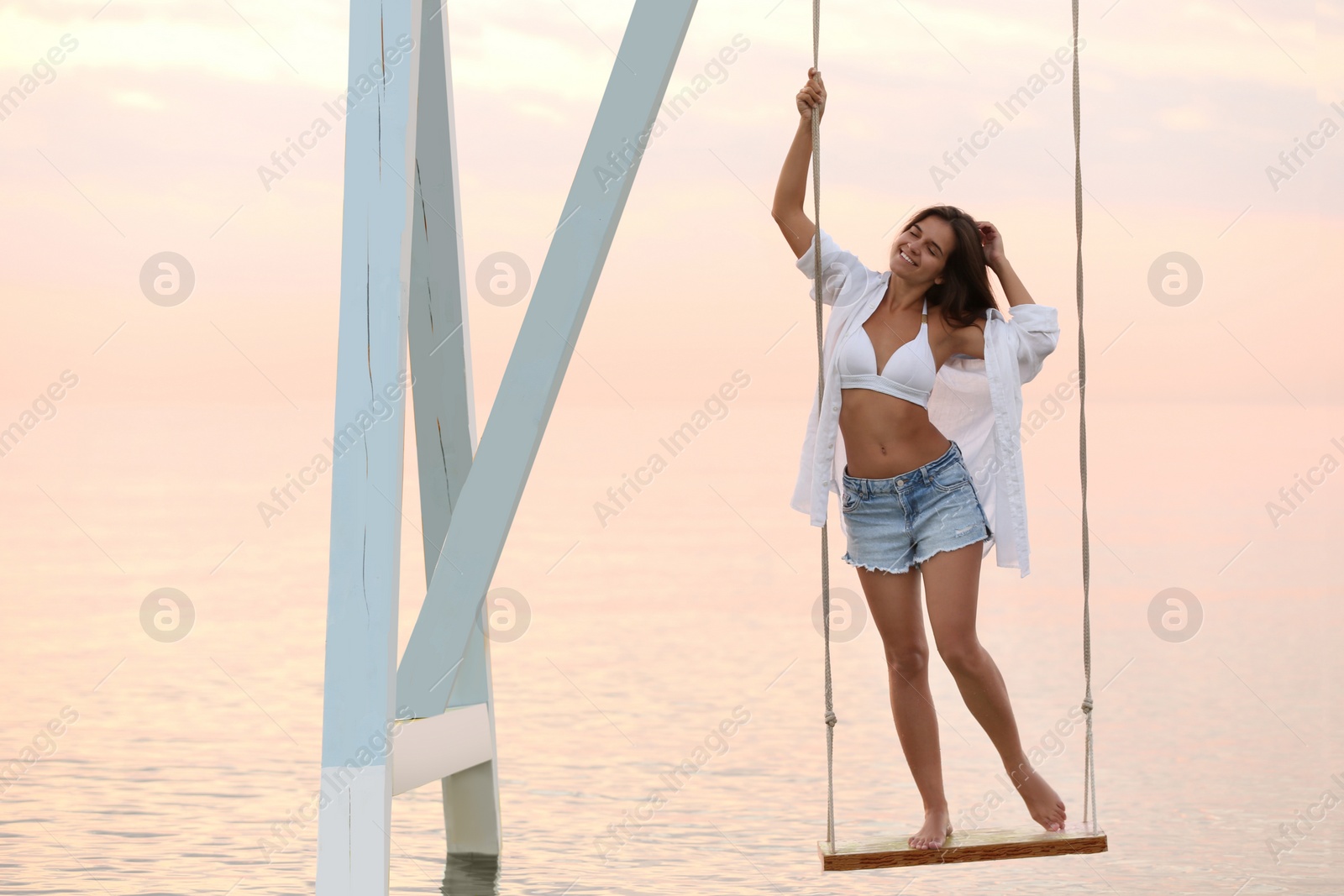Young woman enjoying sunrise on swing over water Photo of Young woman enjoying sunrise on swing over water