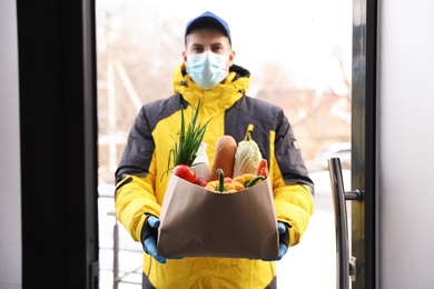 Courier in medical mask holding paper bag with groceries at doorway. Delivery service during quarantine due to Covid-19 outbreak Photo of Courier in medical mask holding paper bag with groceries at doorway. Delivery service during quarantine due to Covid-19 outbreak
