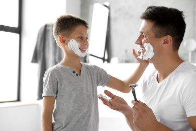 Son applying shaving foam onto father's face in bathroom Photo of Son applying shaving foam onto father's face in bathroom