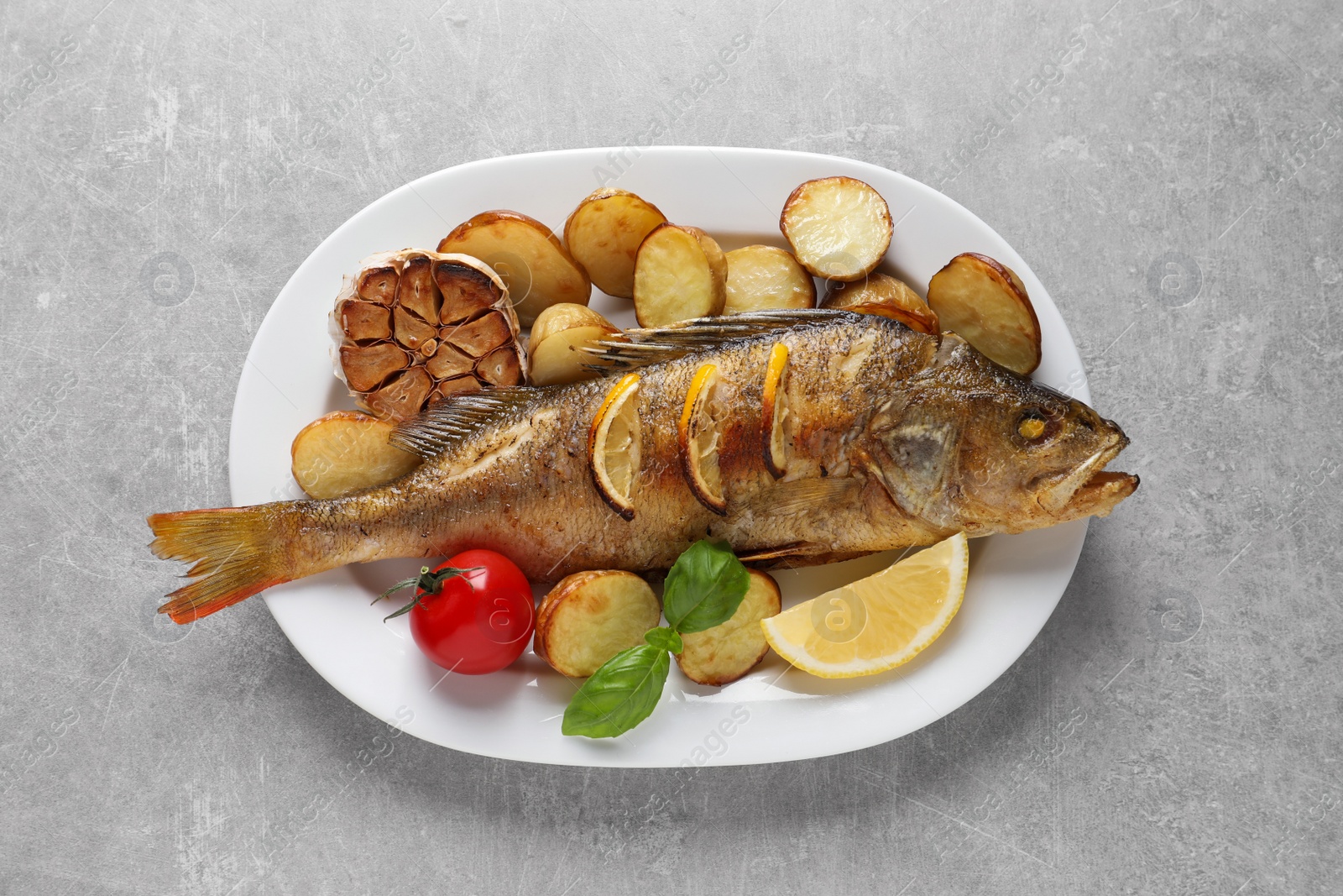 Tasty homemade roasted perch with garnish on grey table, top view. River fish Photo of Tasty homemade roasted perch with garnish on grey table, top view. River fish