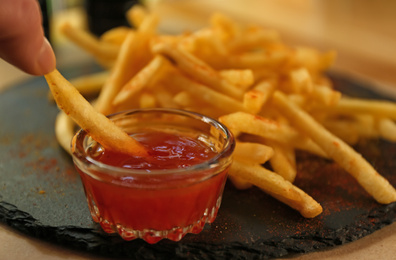 Woman eating tasty french fries with red sauce at table, closeup Photo of Woman eating tasty french fries with red sauce at table, closeup