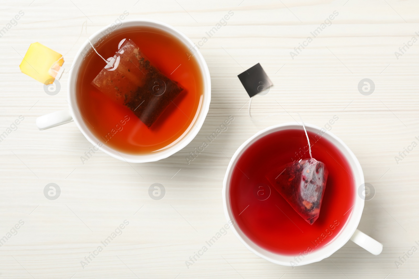 Different tea bags in cups of hot water on white wooden table, flat lay Photo of Different tea bags in cups of hot water on white wooden table, flat lay