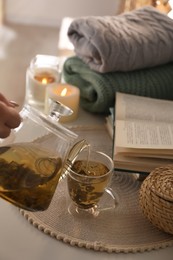 Pouring freshly brewed tea into cup at table in room, closeup. Cozy home atmosphere Photo of Pouring freshly brewed tea into cup at table in room, closeup. Cozy home atmosphere