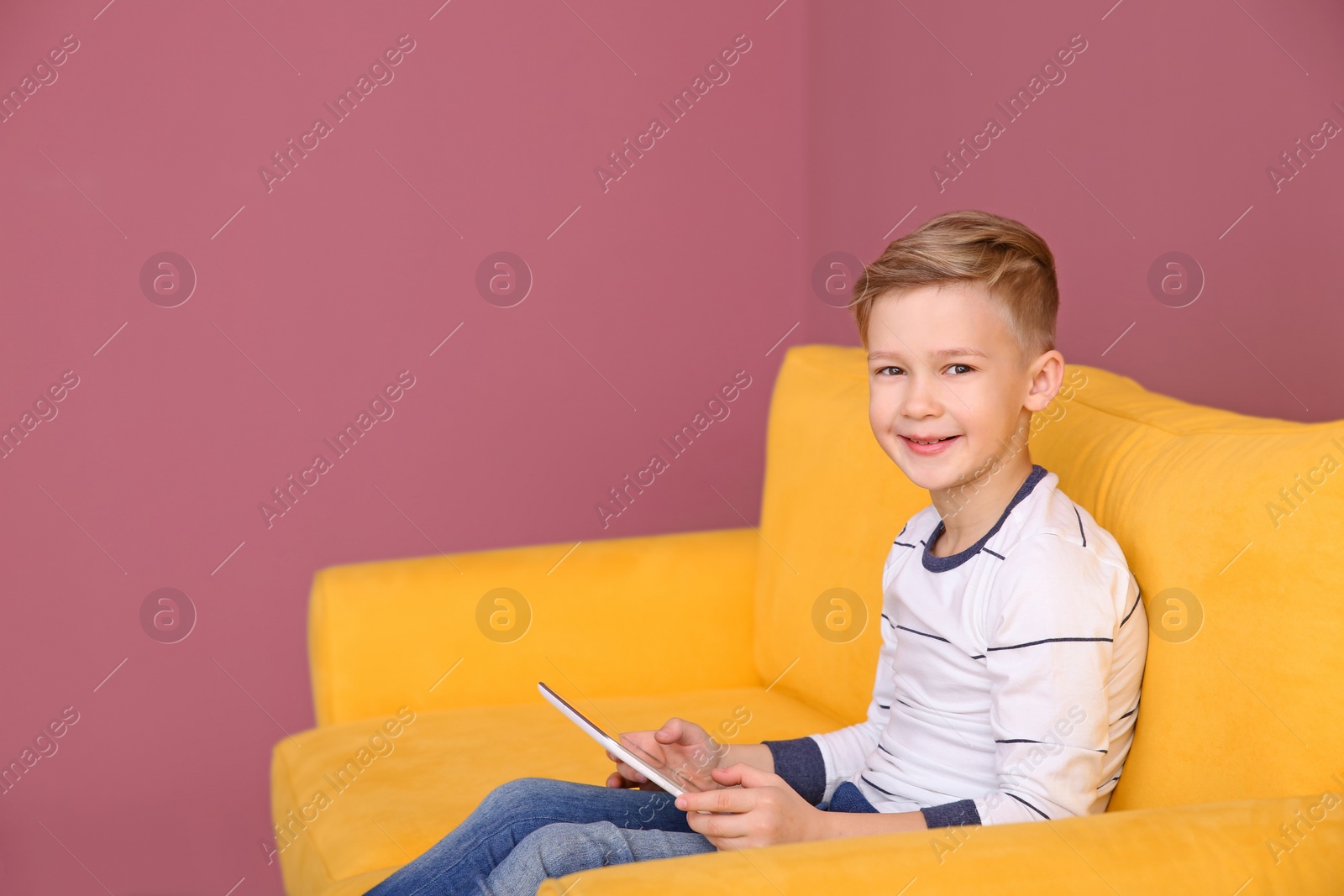 Cute little boy sitting on sofa with tablet computer, indoors Photo of Cute little boy sitting on sofa with tablet computer, indoors