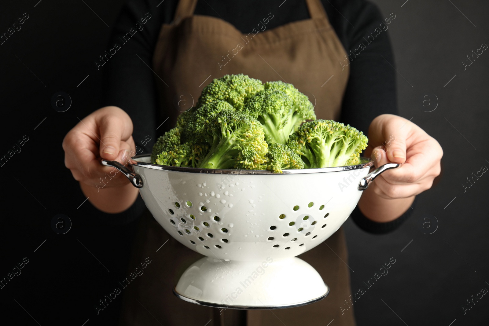 Woman holding colander with fresh green broccoli on black background, closeup Photo of Woman holding colander with fresh green broccoli on black background, closeup