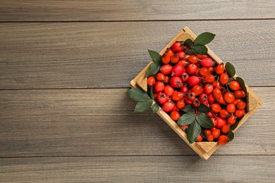 Ripe rose hip berries with green leaves in crate on wooden table, top view. Space for text Photo of Ripe rose hip berries with green leaves in crate on wooden table, top view. Space for text